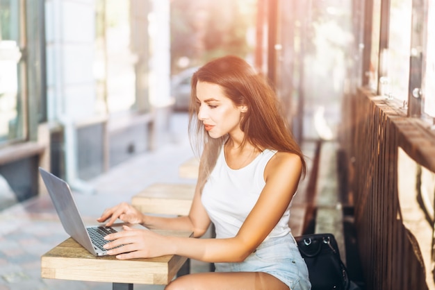 Jolie jeune fille travaillant sur ordinateur portable dans le café de rue en plein air.