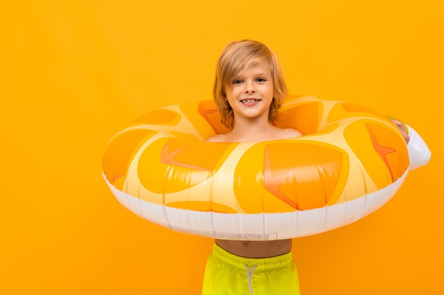 Jolie jeune garçon blond européen en maillot de bain jaune avec cercle de natation ananas sur fond orange