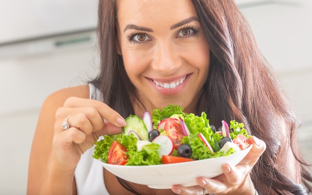 Jolie jeune et heureuse femme mangeant une salade de légumes.