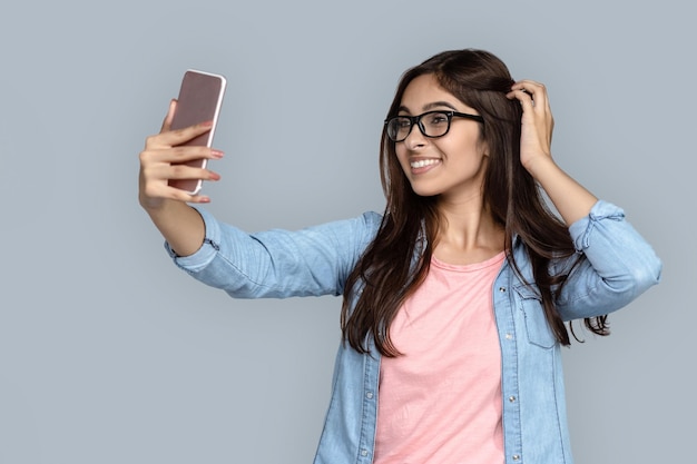 Une jolie jeune Indienne porte des lunettes avec un smartphone moderne pour faire un selfie.