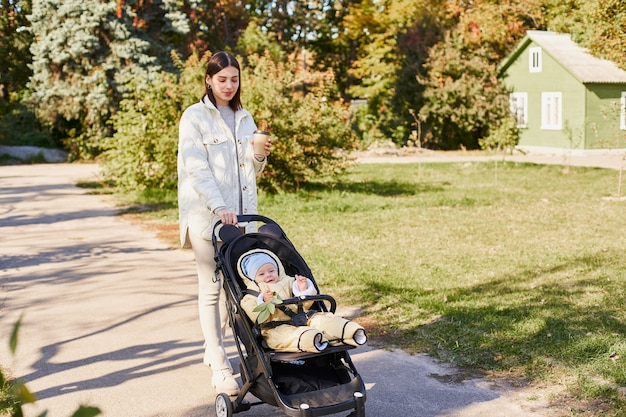 Jolie jeune mère se promène dans le parc en automne avec son fils dans une poussette