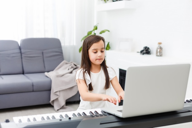 Jolie jeune musicienne jouant du piano numérique classique à la maison pendant les cours en ligne à la maison, distance sociale pendant la quarantaine, auto-isolement, concept d'éducation en ligne