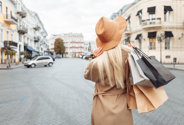 Jolie jolie femme accro du shopping en manteau d'automne et chapeau tenant de nombreux sacs à provisions en papier dans la ville européenne