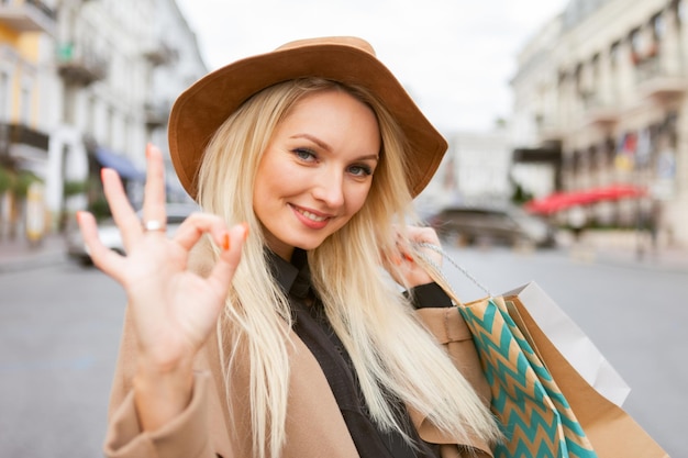 Jolie jolie femme accro du shopping en manteau d'automne et chapeau tenant de nombreux sacs à provisions en papier dans la ville