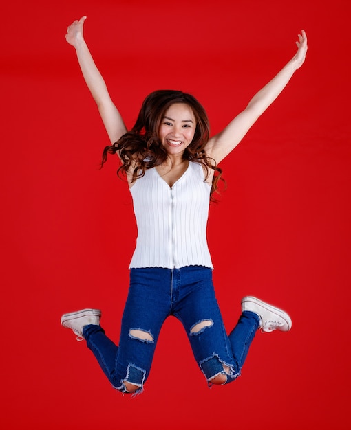 Jolie et jolie femme asiatique aux cheveux noirs se sentant excitée et saute en l'air avec drôle et gai pour la publicité et l'utilisation de bannières, arrêtez le mouvement isolé sur fond rouge vif.