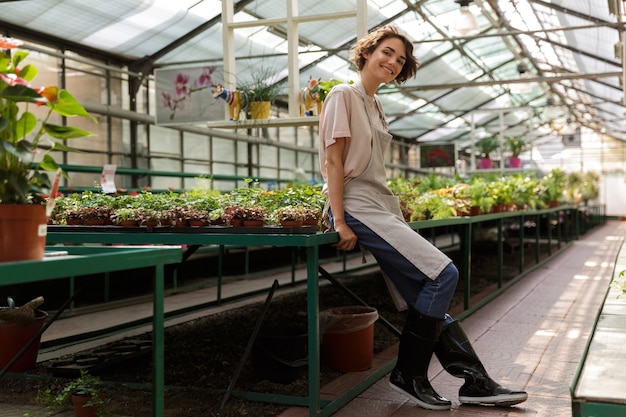 Jolie jolie femme jardinier debout sur les plantes à fleurs en serre