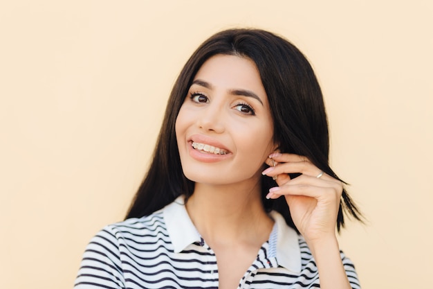 Jolie jolie femme a un large sourire, des cheveux noirs, garde la main sur l'oreille