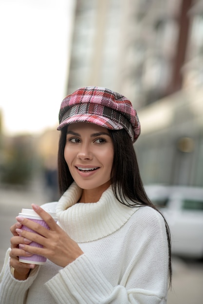 Jolie jolie femme tenant une tasse tout en buvant du café dans la rue