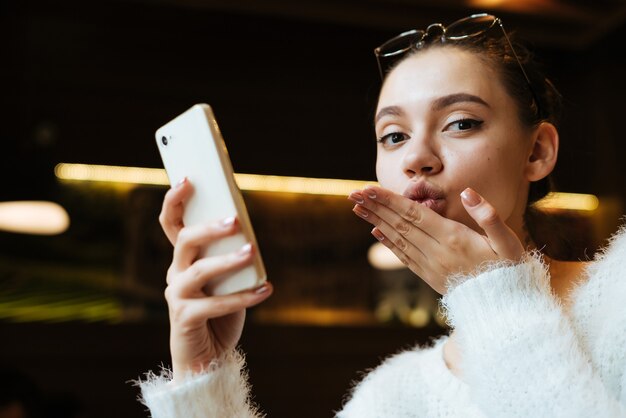 Jolie jolie fille assise dans un café, tenant un smartphone et pensant au travail