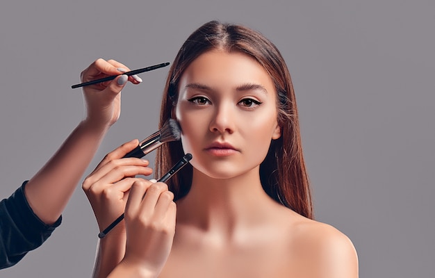 Jolie jolie fille avec des pinceaux de maquillage isolés sur fond gris.