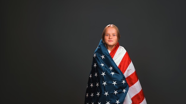 Jolie jolie petite fille enveloppée dans un drapeau USA célèbre le jour de l'indépendance exprime le patriotisme isolé sur le mur noir