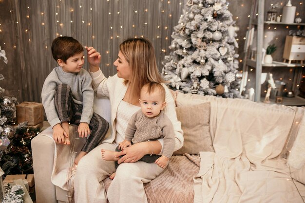 Une jolie maman blonde avec ses fils est assise sur le canapé dans la chambre dans une atmosphère de nouvel an