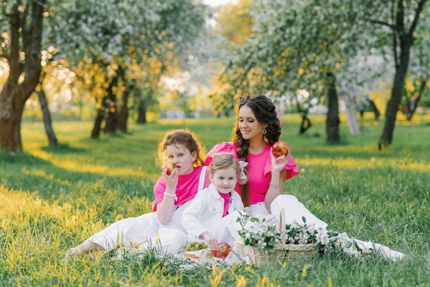 Jolie maman et ses deux filles pique-niquent dans le jardin de printemps Activité de plein air Moments doux