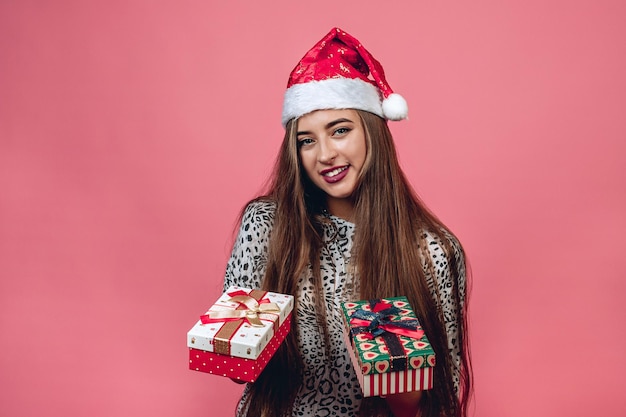 Jolie mannequin parfaitement maquillée portant une tenue décontractée et un chapeau de père Noël tenant deux coffrets cadeaux dans ses mains. Concept de vacances de Noël.