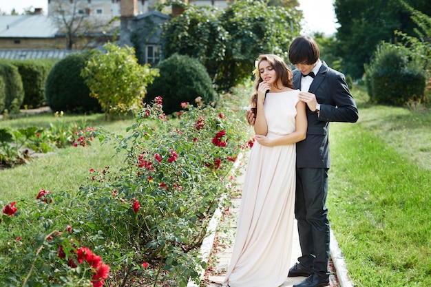 Jolie mariée aux longs cheveux bouclés et marié debout au fond de parc vert, photo de mariage, beau couple, jour de mariage, portrait.