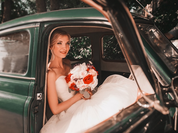 Photo jolie mariée avec le bouquet assis dans une voiture ancienne. mariage dans un style rétro