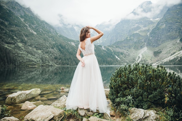 Jolie mariée brune en robe de mariée blanche magnifique debout près du lac Morskie Oko