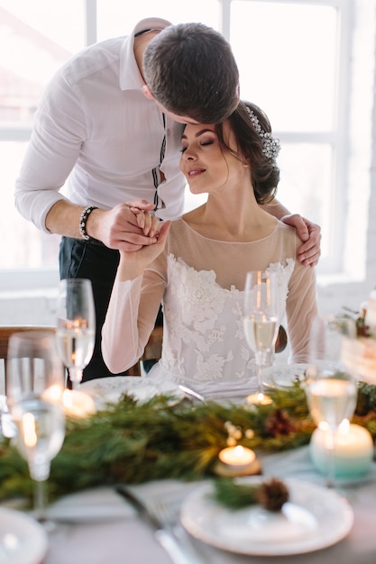 Jolie mariée et le marié près de la table de mariage avec un gâteau de mariage, des bougies bleues et des décorations en pin