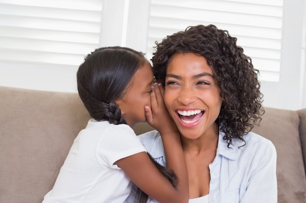 Jolie mère assise sur le canapé avec sa fille chuchotant un secret