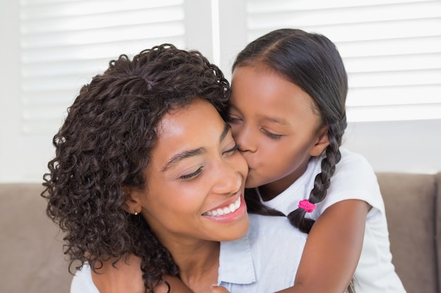 Jolie mère assise sur le canapé avec sa fille embrassant sa joue