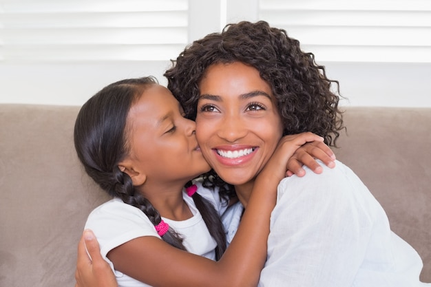 Jolie mère assise sur le canapé avec sa fille embrassant sa joue