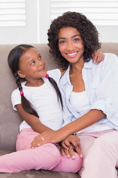 Jolie mère assise sur le canapé avec sa fille souriant à la caméra