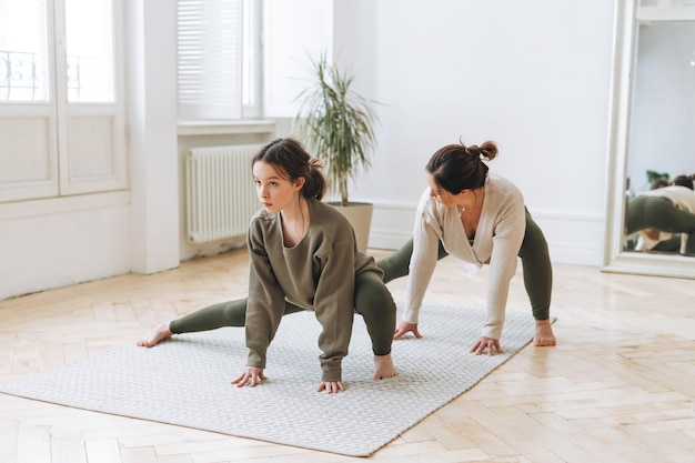 Jolie mère femme d'âge moyen et fille adolescente ptactice yoga ensemble dans la salle lumineuse