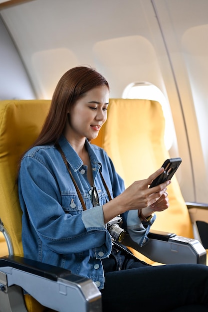 Une jolie passagère asiatique assise dans un siège de classe économique se détend sur un smartphone