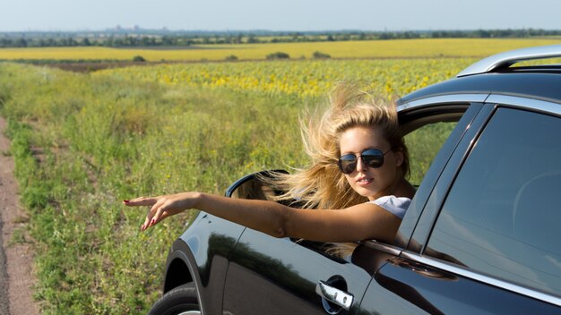 Jolie passagère blande se penchant hors d'une fenêtre de voiture donnant un signal de la main pour tourner sur la route