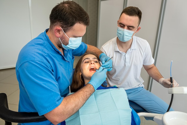 Jolie patiente assise dans un fauteuil pendant que le médecin avec un assistant examinant ses dents Concept de stomatologie