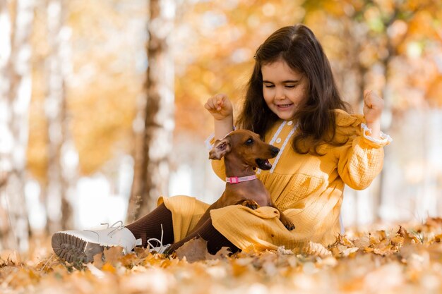 Une jolie petite brune se promène à l'automne avec un dachshund dans le parc.