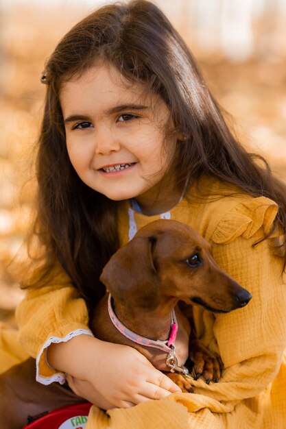 Une jolie petite brune se promène à l'automne avec un dachshund dans le parc.