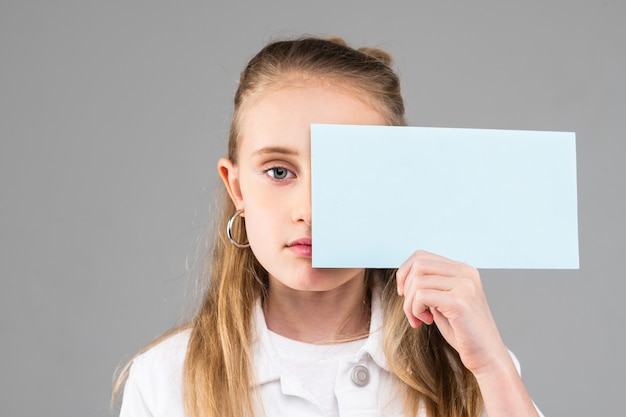 Jolie petite dame aux cheveux longs aux yeux bleus tenant du papier vide et couvrant la moitié de son visage