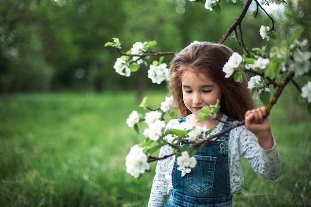 Une jolie petite fille de 5 ans dans un verger de pommiers blancs en fleurs au printemps. Printemps, verger, floraison, allergie, parfum printanier, tendresse, soin de la nature. Portrait