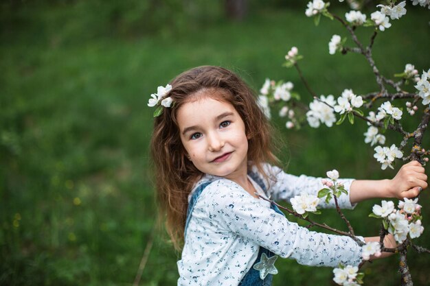 Une jolie petite fille de 5 ans dans un verger de pommiers blancs en fleurs au printemps. Printemps, verger, floraison, allergie, parfum printanier, tendresse, soin de la nature. Portrait