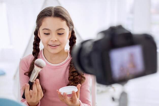 Jolie petite fille agissant comme une maquilleuse devant la caméra