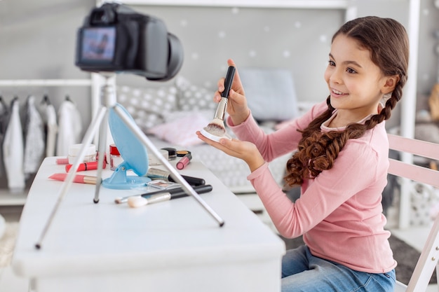 Jolie petite fille agissant comme une maquilleuse devant la caméra