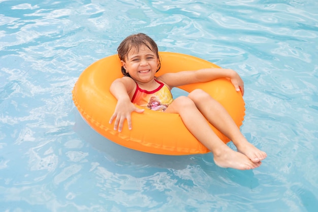 Jolie petite fille à l'aide d'un flotteur gonflable orange dans la piscine heureuse de profiter de vacances
