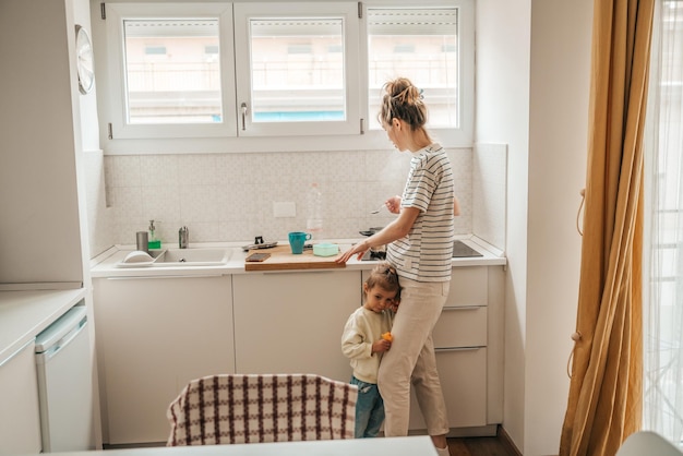 Jolie petite fille appuyée contre la mère qui prépare le petit-déjeuner pour elle le matin