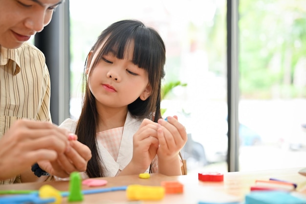 Jolie petite fille asiatique apprenant à mouler l'argile de son professeur d'art à la salle de jeux de l'école