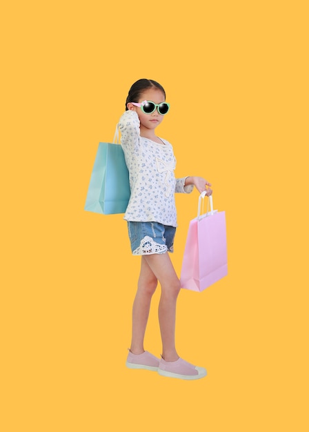 Jolie petite fille asiatique enfant portant des lunettes de soleil tenant des sacs sur jaune