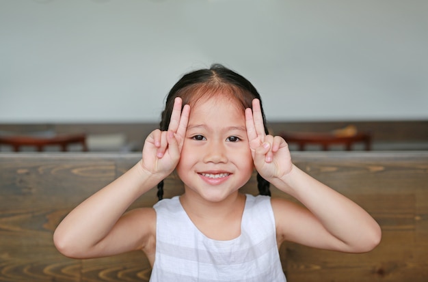 Jolie petite fille asiatique avec une expression semblable à un lapin allongé sur la table en bois avec regarder la caméra