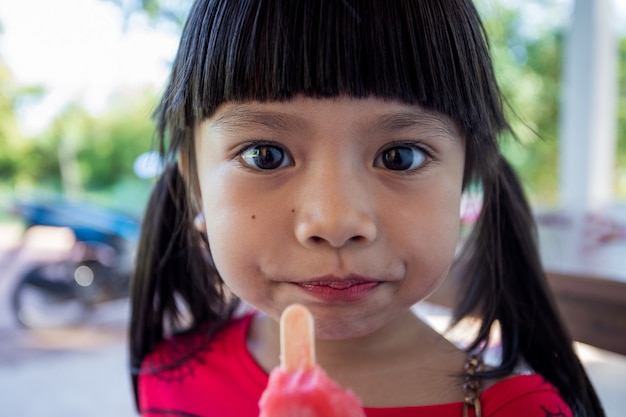 La jolie petite fille asiatique mange joyeusement de la glace.