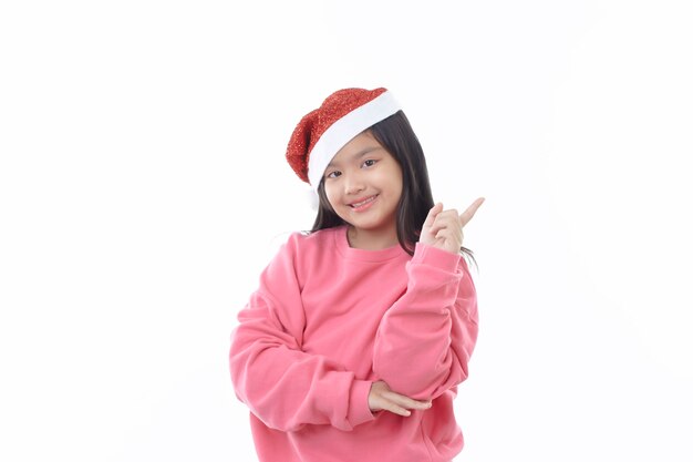 Une jolie petite fille asiatique portant un chapeau de père Noël pointant vers le haut sur blanc