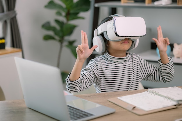 Une jolie petite fille asiatique portant des lunettes VR avec un ordinateur portable placé sur la table dans la classe de technologie STEM Éducation en ligne Érudition