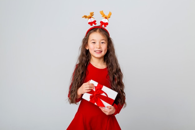 jolie petite fille asiatique vêtue d'une robe rouge tient une boîte-cadeau sur l'espace de texte de concept de noël en arrière-plan