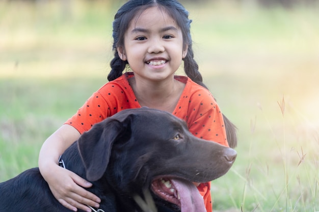 Une jolie petite fille d'Asie du Sud-Est vêtue de tenues rouges joue avec son gros chien dans la cour arrière ou avant le soir. Concept d'amoureux des animaux de compagnie