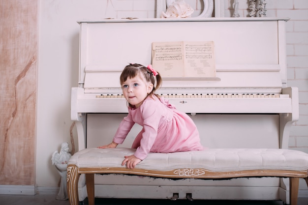 Jolie petite fille assise près du piano à la maison