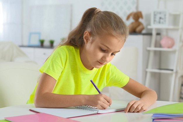 Jolie petite fille assise à table et faisant des tâches ménagères