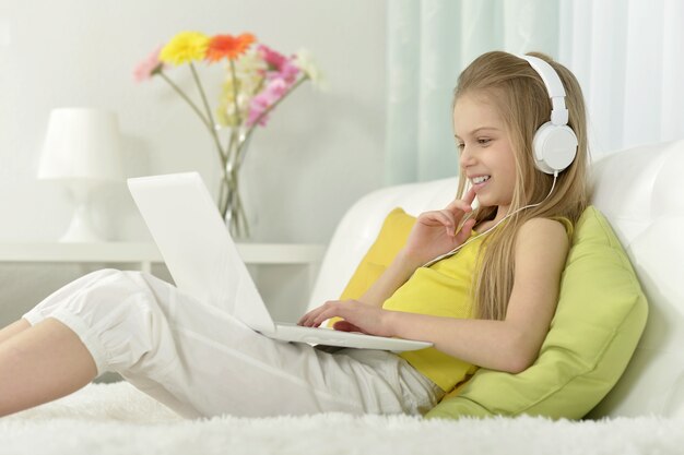 Jolie petite fille au casque avec ordinateur portable à la maison